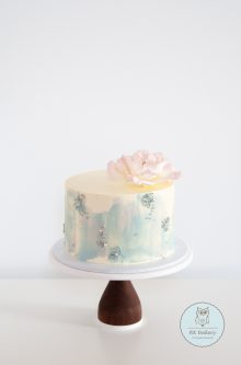 Light blue cake with sugar rose on top and sprinkles on the side