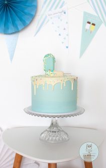 Light blue birthday cake with melting sugar ice cream sticks on top and birthday decorations in the background