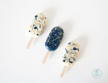 Three white and navy blue painted cakesicles with paint-drop like decorations